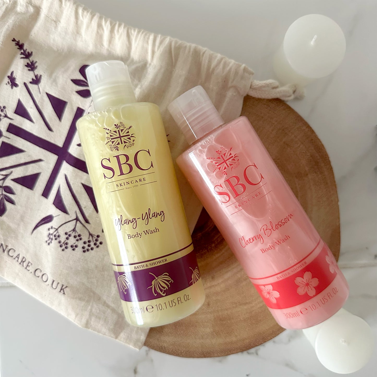 Ylang-Ylang Body Wash and Cherry Blossom Body wash on a slice of wood with candles