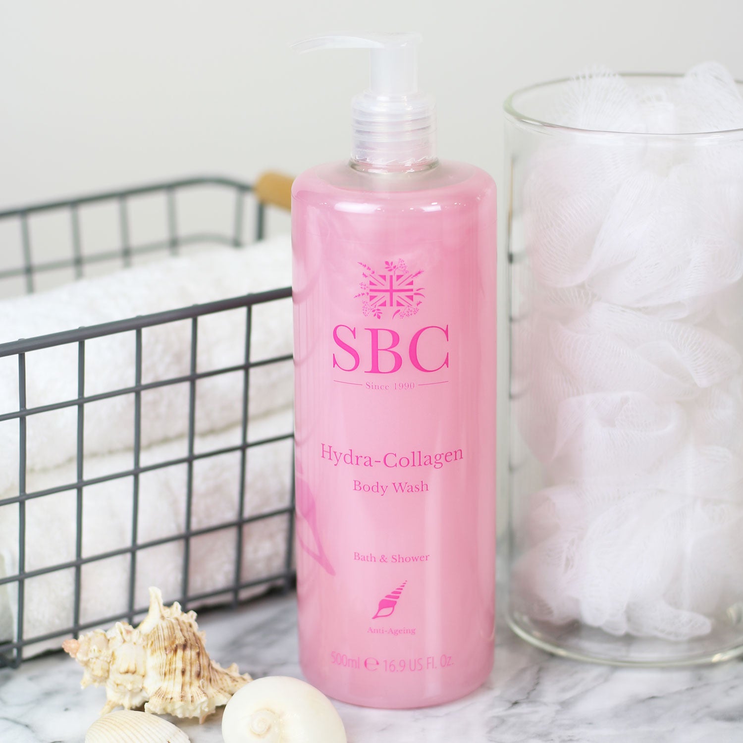 500ml of SBC Skincare's Hydra-Collagen Body Wash  on a marble counter with towels and shower scrunchies