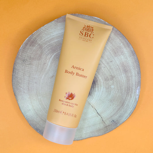 SBC Skincare Amica Body Butter tube on a textured stone surface with a yellow background