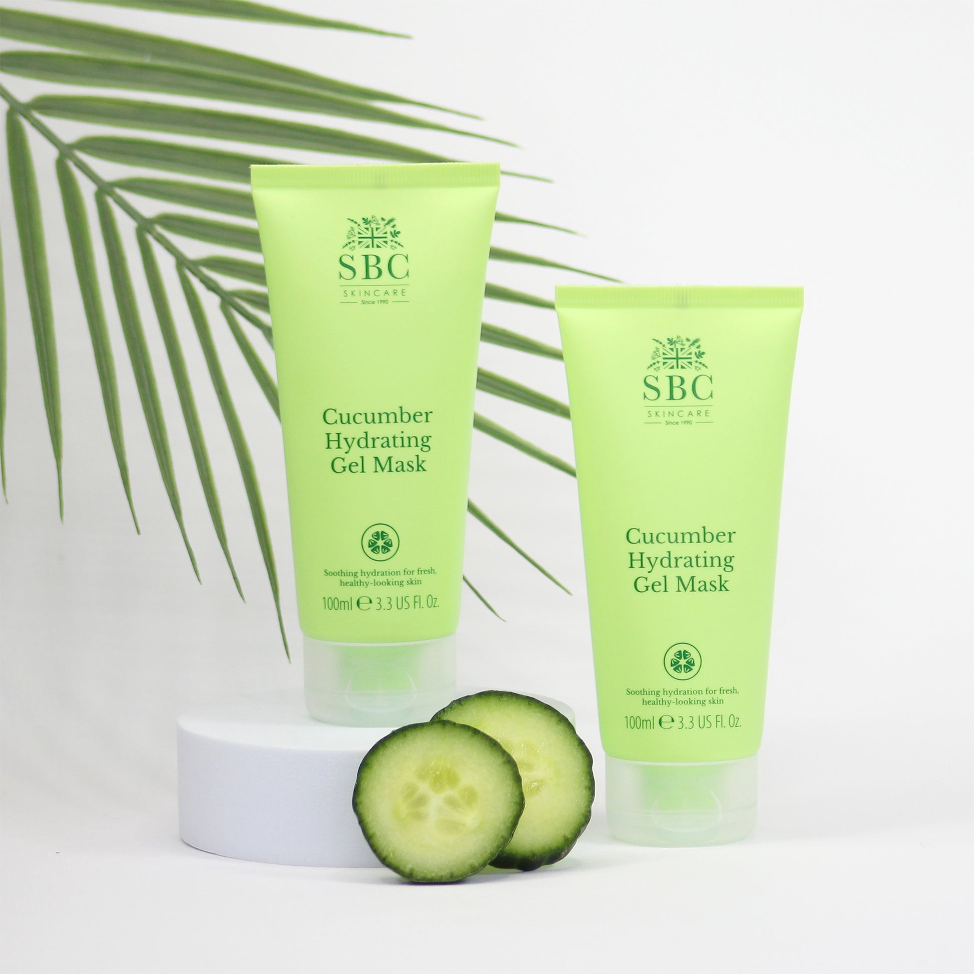 Lifestyle image of two bottles of SBC Cucumber Hydrating Gel Mask with cucumber slices on a white background