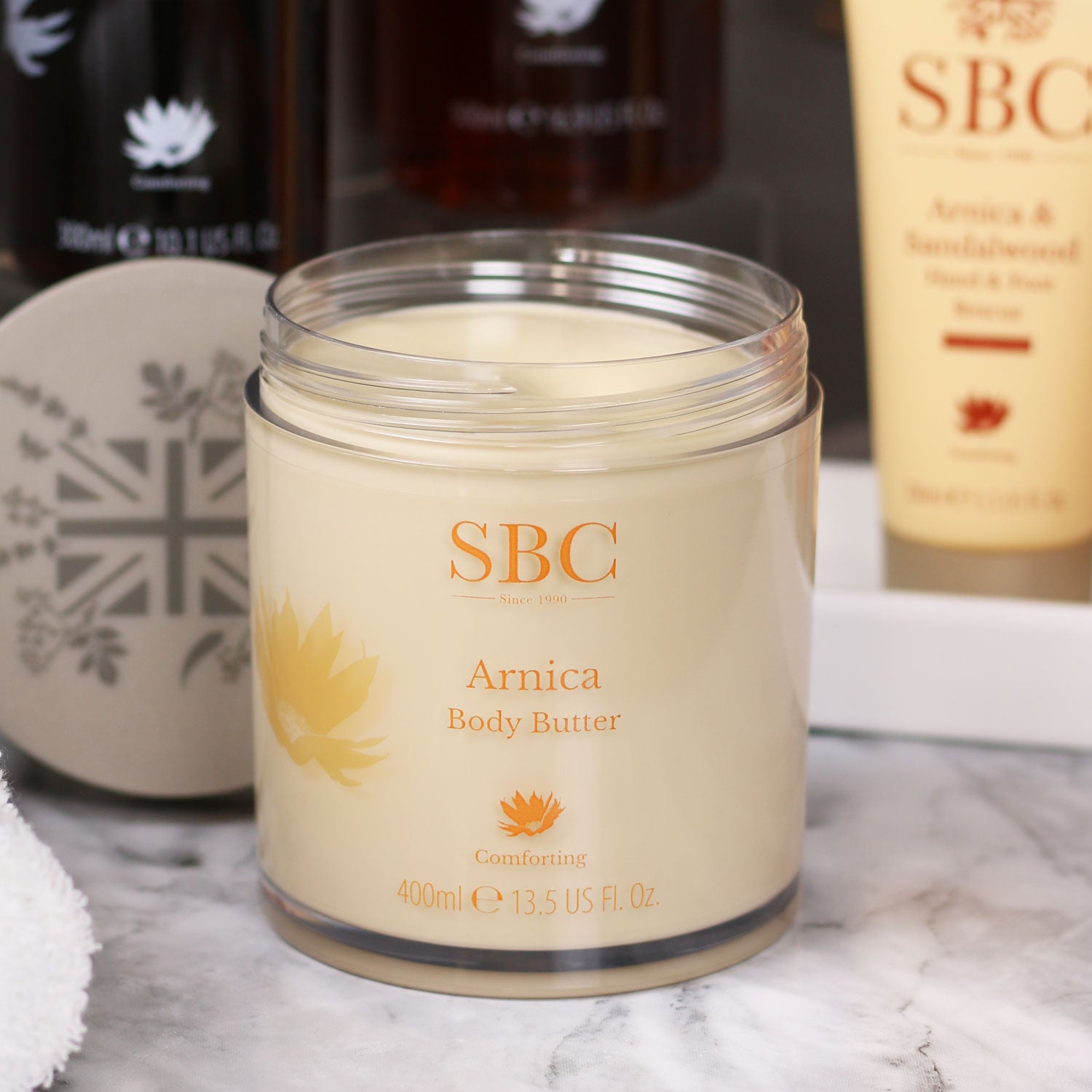 Arnica Body Butter on a marble table top with other Arnica products behind