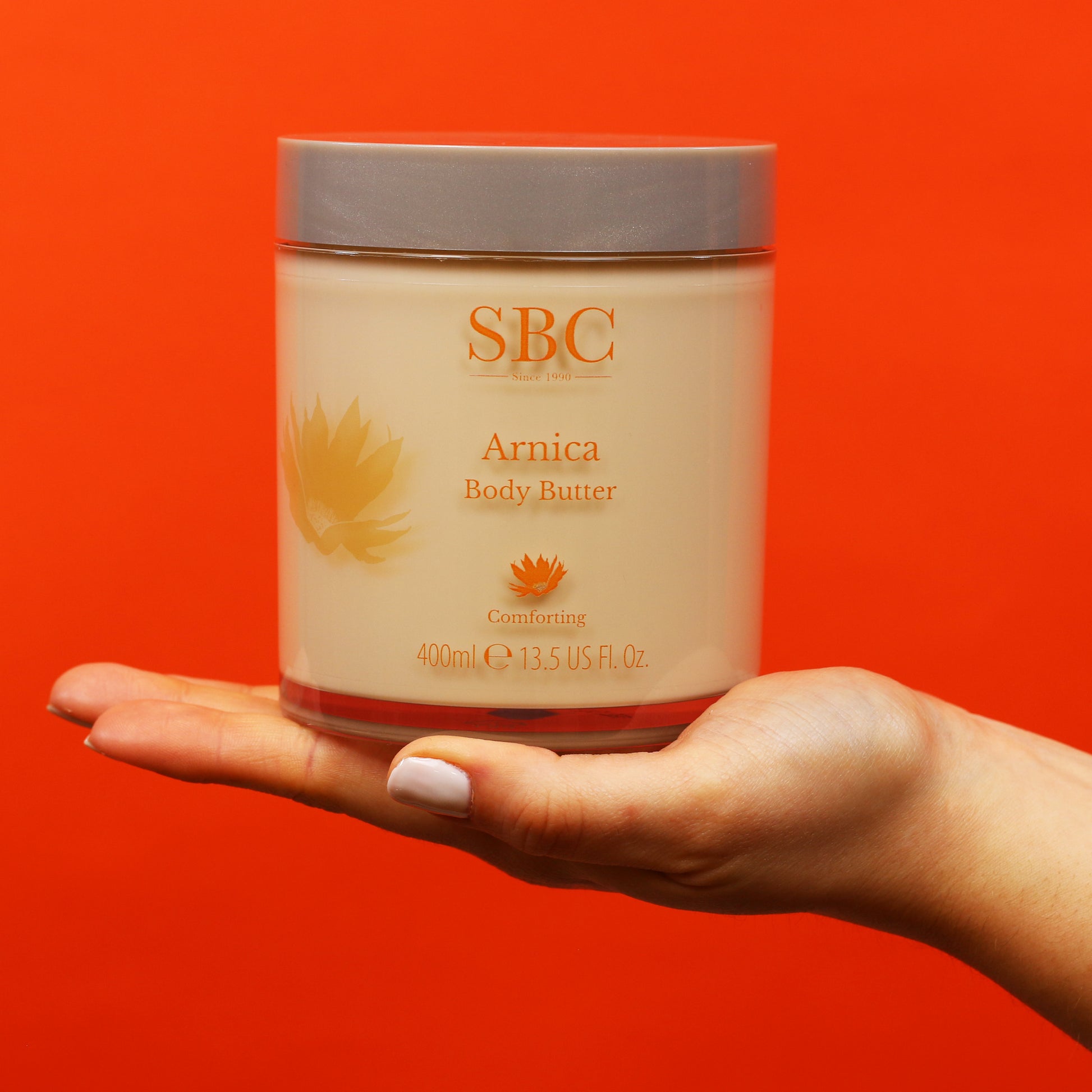 Arnica Body Butter being held on a flat palm on a bright red background 
