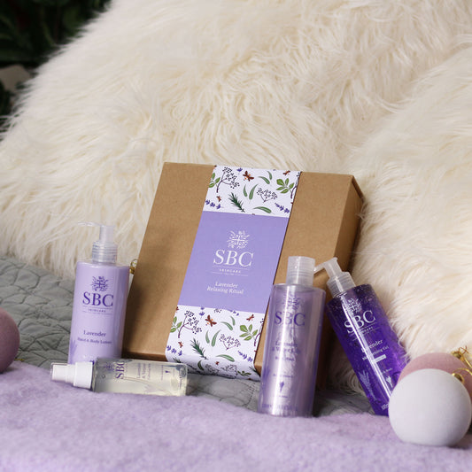 SBC Skincare’s Lavender Relaxing Ritual on a bed with a purple blanket and fluffy cream cushions 