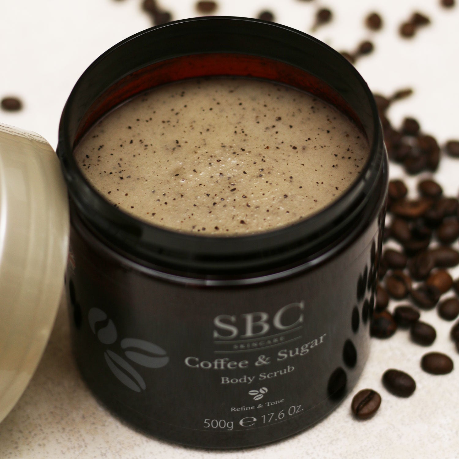 Coffee & Sugar Body Scrub 500g with lid open and coffee beans sprinkled around the base