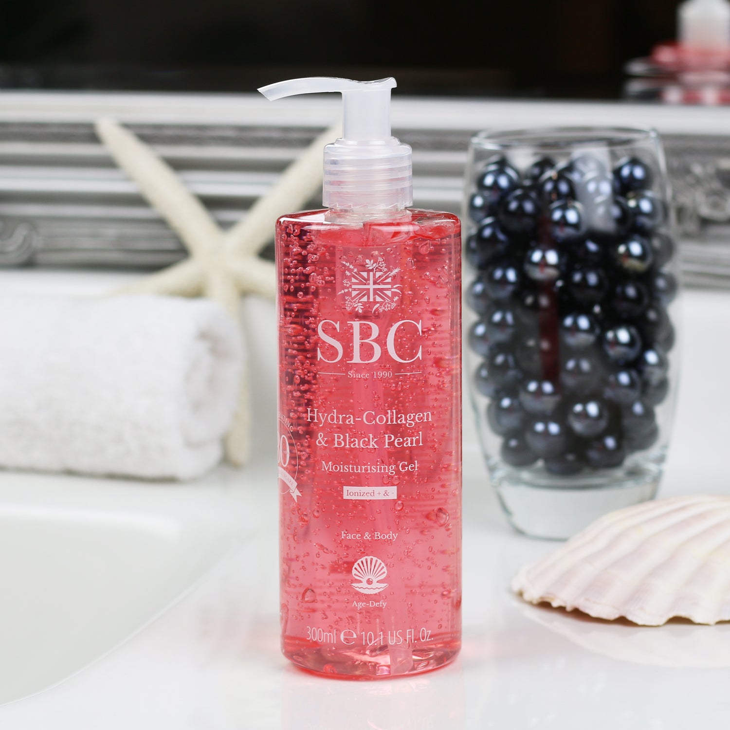 300ml of SBC Skincare's Hydra-Collagen & Black Pearl Moisturising Gel on a bathroom sink with a glass of black pearls and a shell 