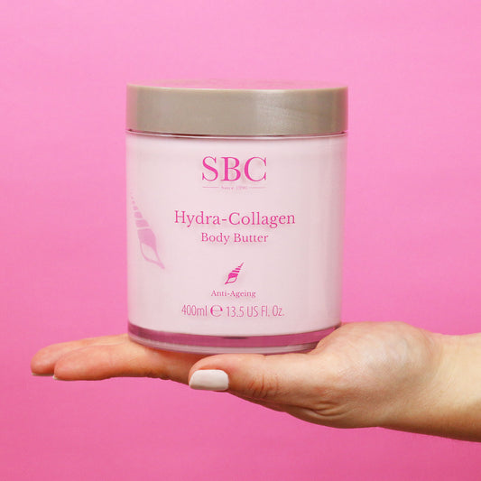 Hydra-Collagen Body Butter on the palm of a hand with a pink background 