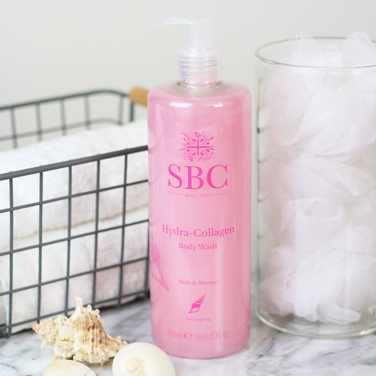 500ml of SBC Skincare's Hydra-Collagen Body Wash  on a marble counter with towels and shower scrunchies 