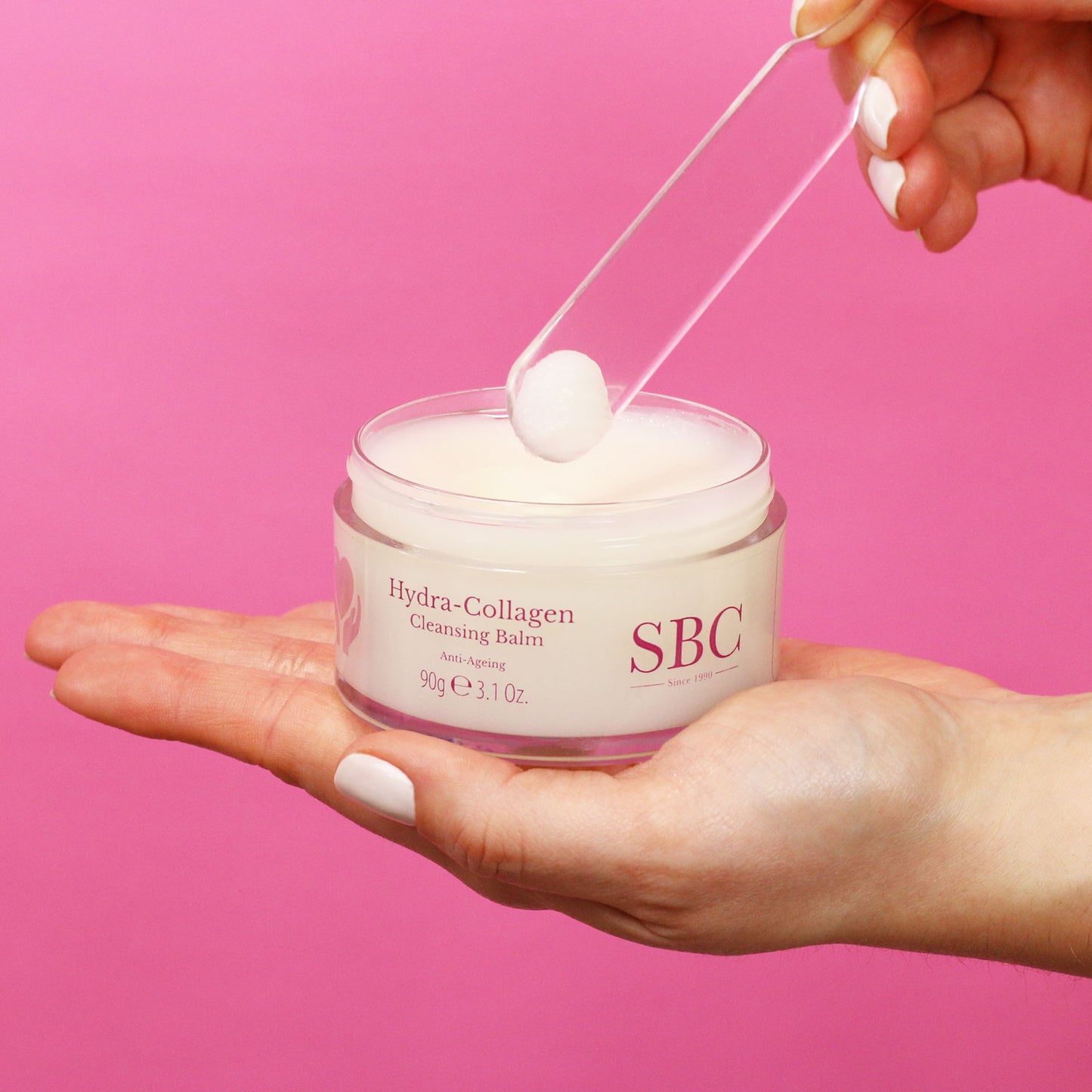 Hydra-Collagen Cleansing Balm on a plastic spatula on a bright pink background 
