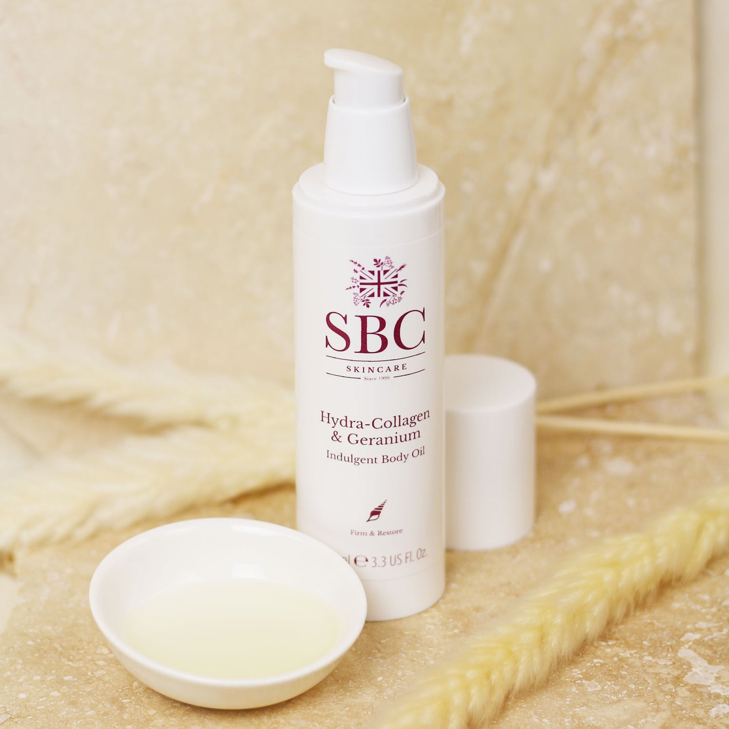 Hydra-Collagen & Geranium Body Oil on stone tiles with a dish of the oil decanted 
