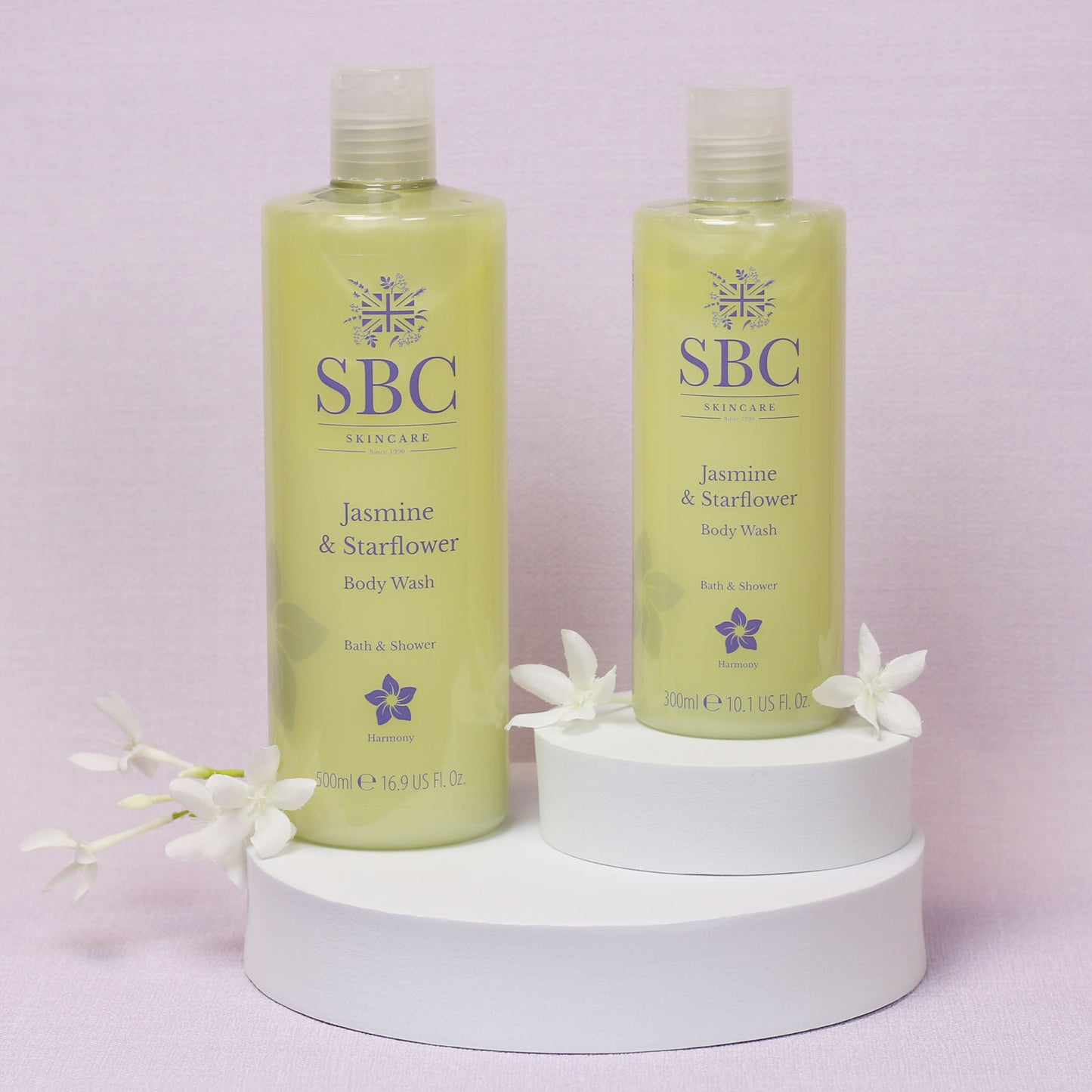 300ml and 500ml SBC Jasmine & Starflower Body Wash on white platforms with jasmine flowers