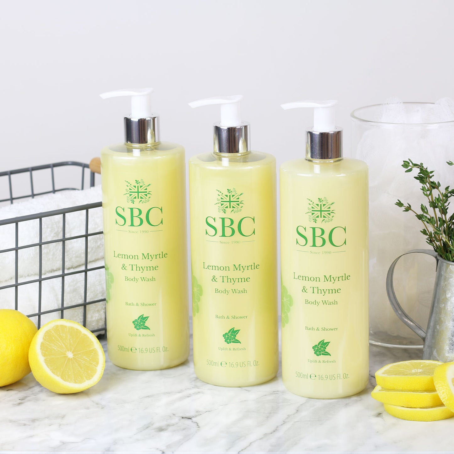 three 500ml Lemon Myrtle & Thyme Body Washes  on a marble counter with lemon wedges and white towels