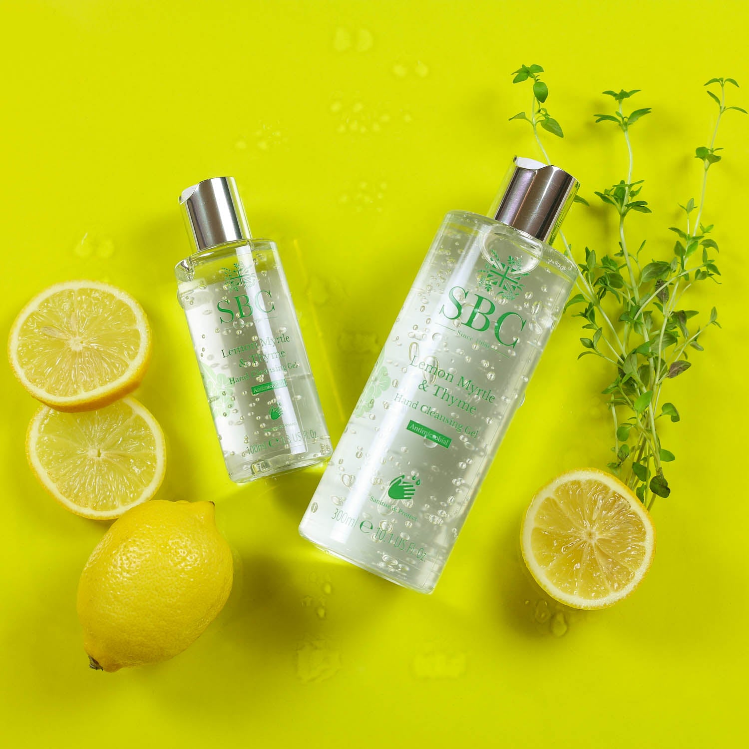 100ml and 300ml Lemon Myrtle & Thyme Hand Cleansing Gel on a bright yellow background with sliced lemons and herbs 