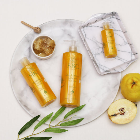 100ml, 300ml and 500ml Manuka Honey & Quince Body Washes on marble trays with honey comb and quinces 