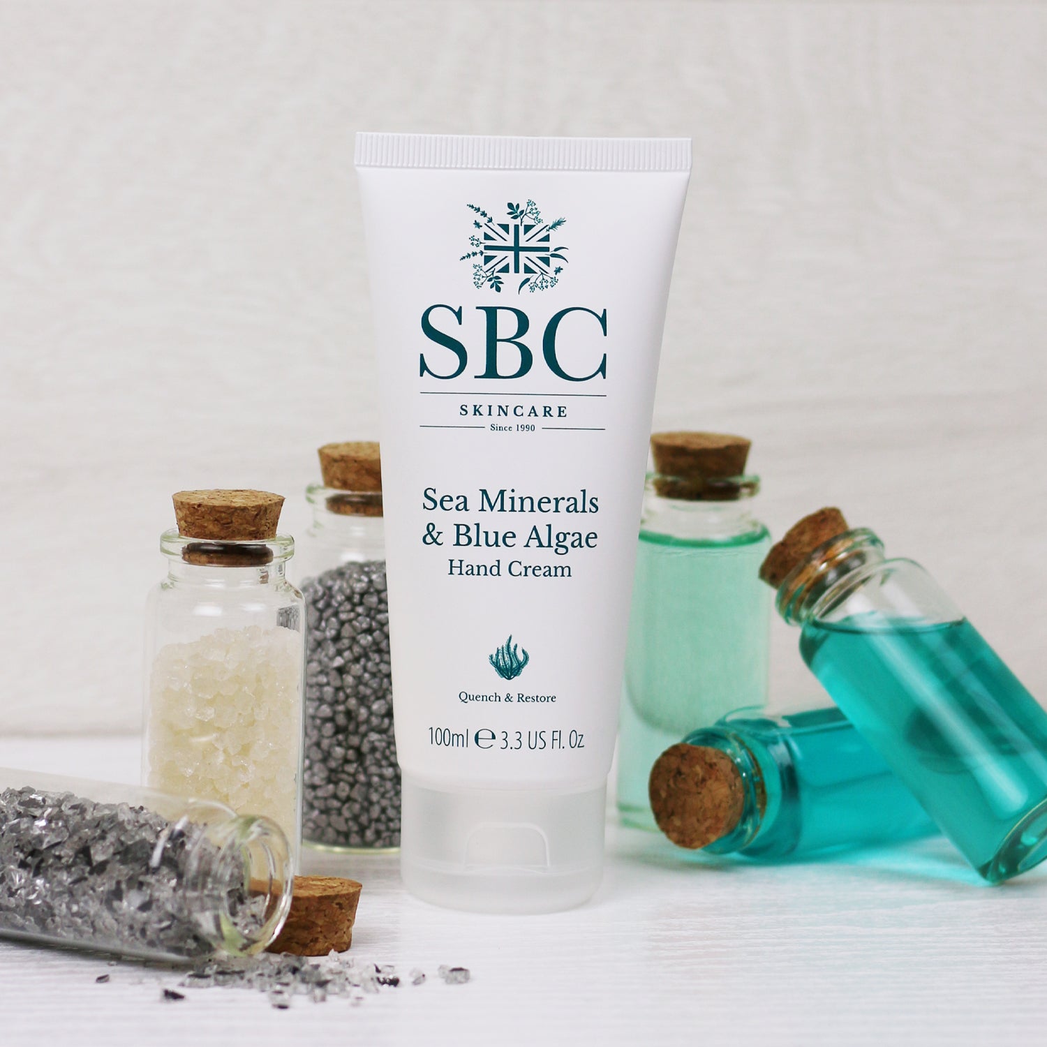 Sea Minerals & Blue Algae Hand Cream on a white counter with tiny glass vials of minerals 