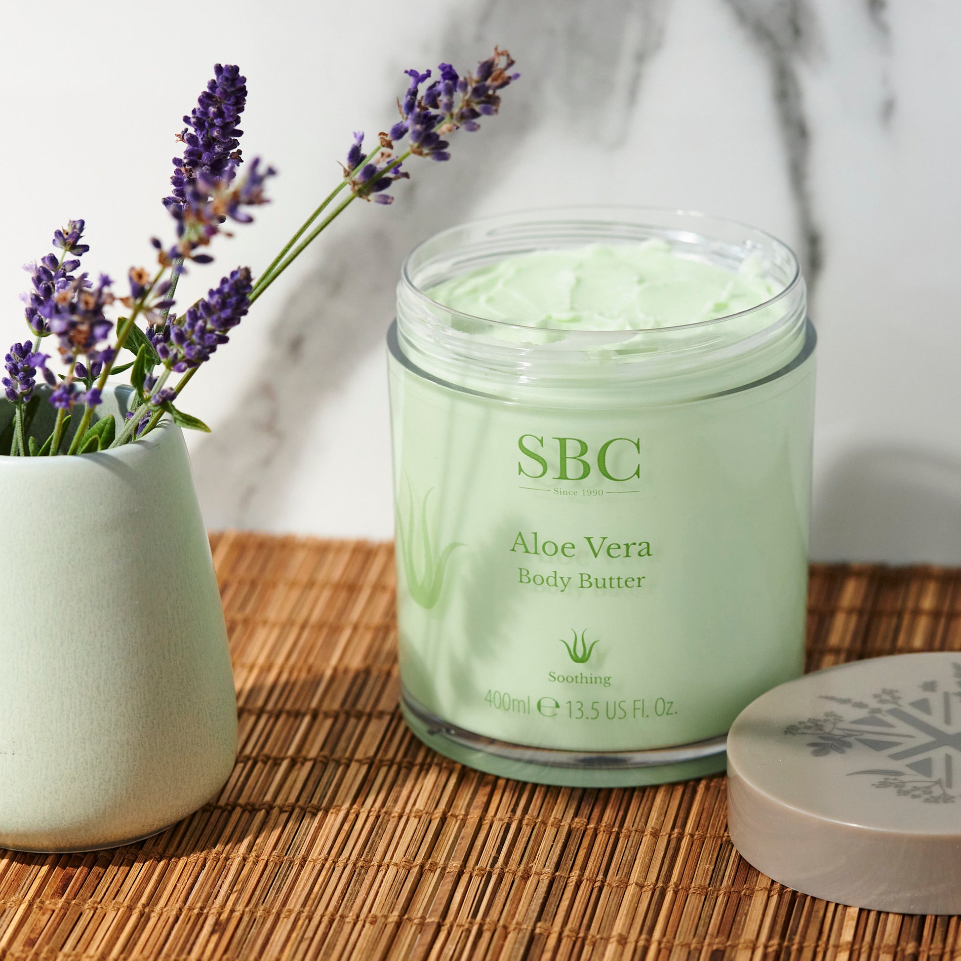 Aloe Vera Body Butter on a wooden matt with a marble background and pot of lavender 