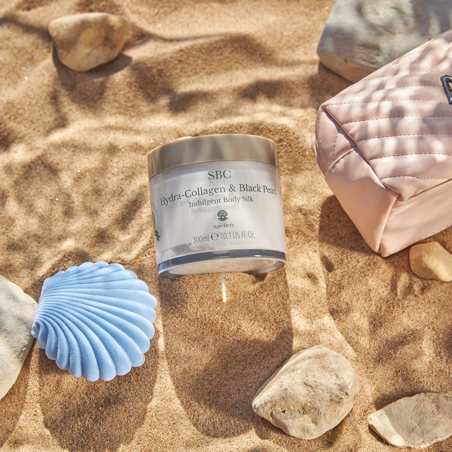 Hydra-Collagen & Black Pearl Indulgent Body Silk in the sand with shells and stones 