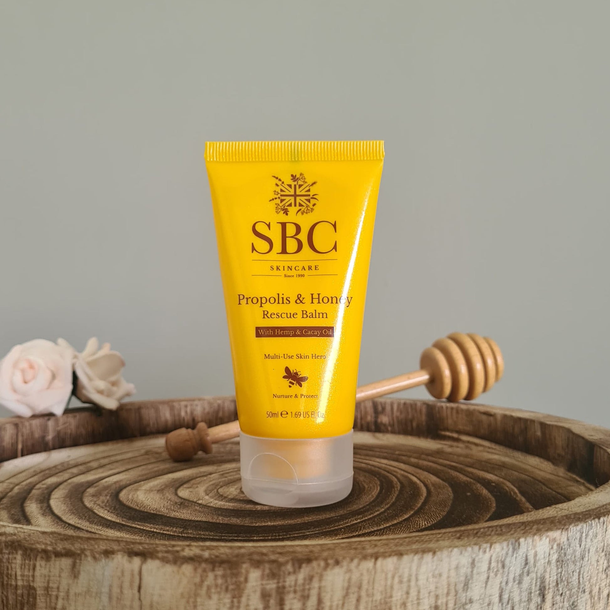 Propolis & Honey Rescue Balm on a wooden stand with flowers